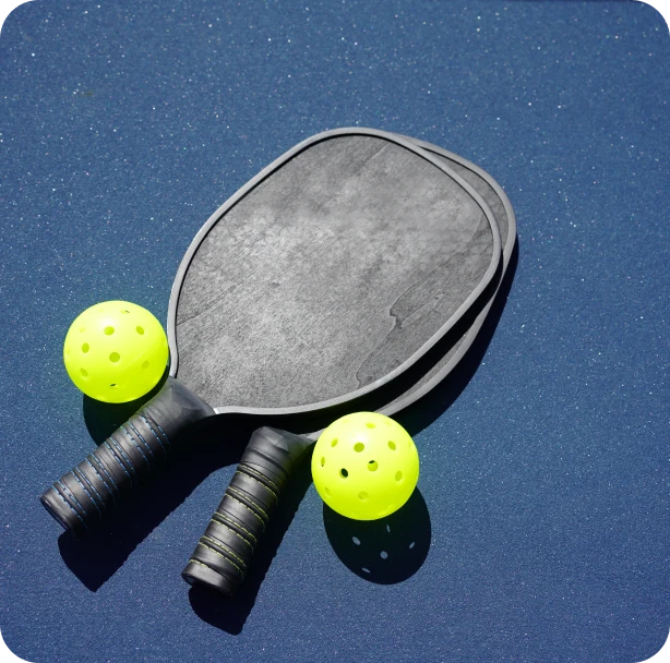 Two pickleball rackets and pickleballs laying on a navy blue court at Blumenthal Farms.