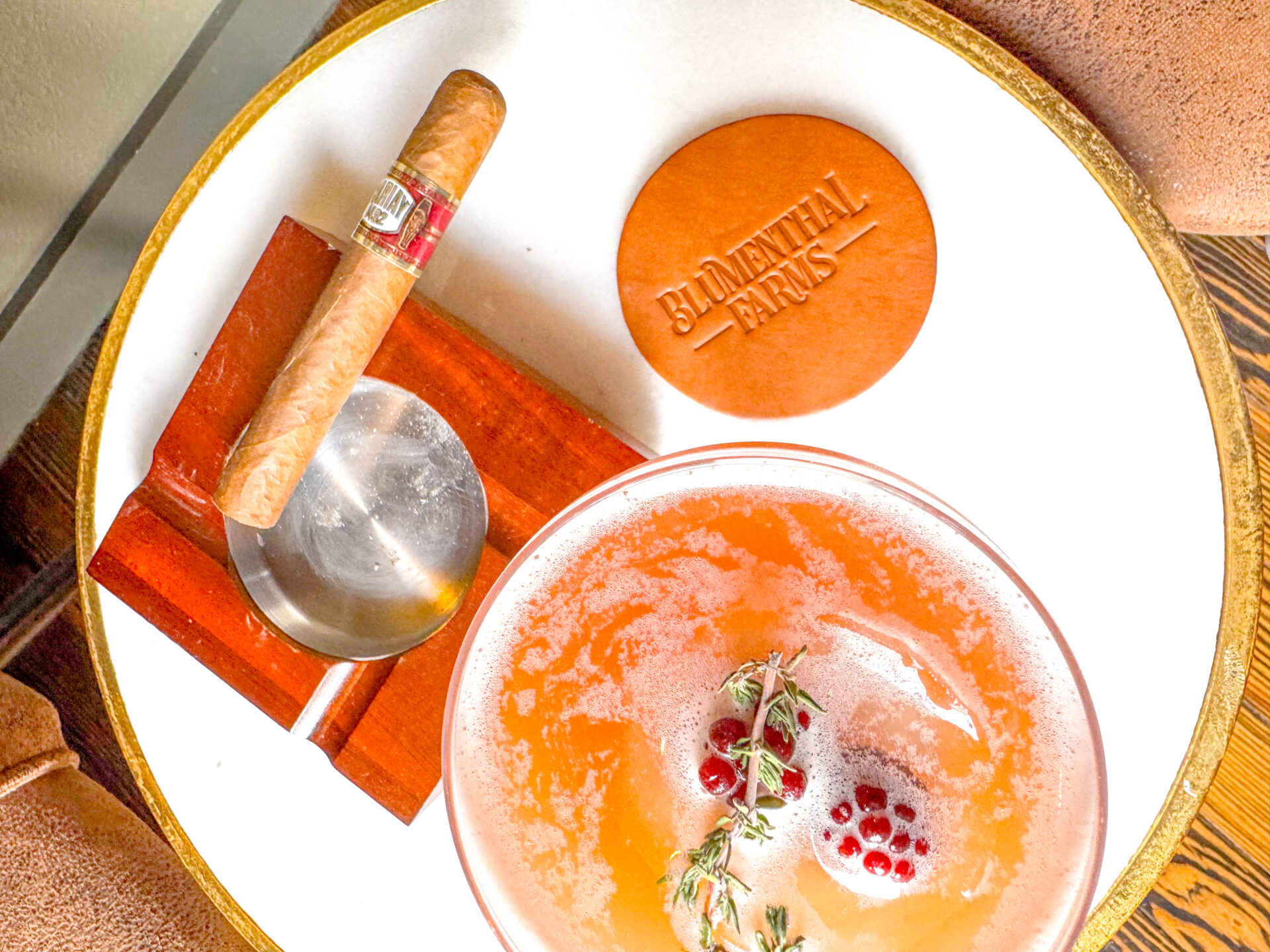 A cocktail and cigar sitting on an ash tray with a branded coaster sit on a table.