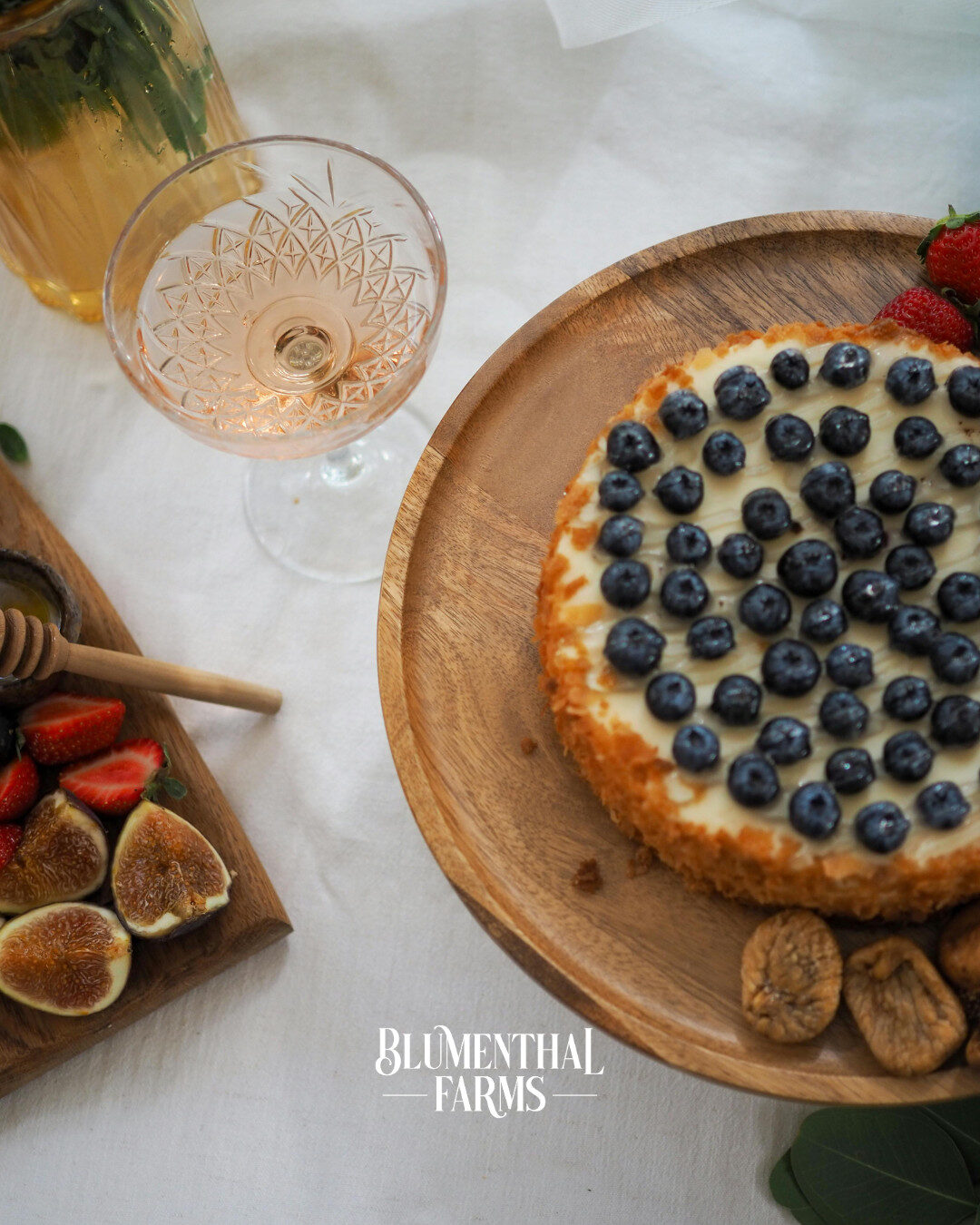 A cheesecake topped with blueberries and a wine glass on a table.
